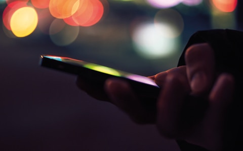 close up of a hand holding a smart phone with lights blurred out in the background