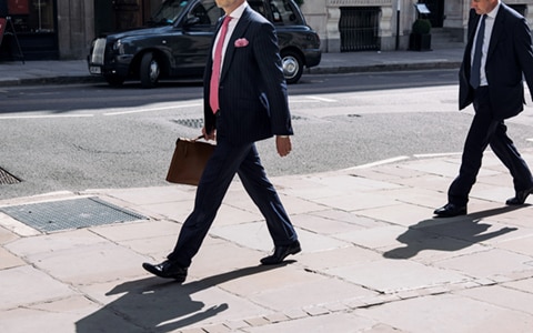 the bottom half of two men walking in suits with briefcases