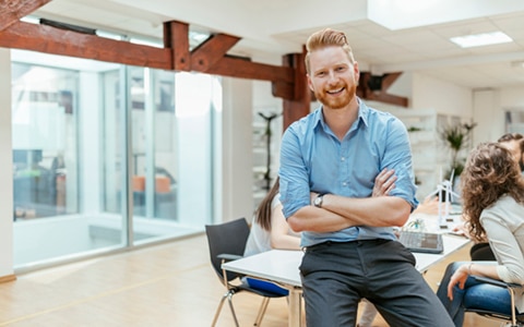 man sitting on desk with arms crossed smiling