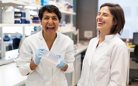 two women in whote lab coats laughing