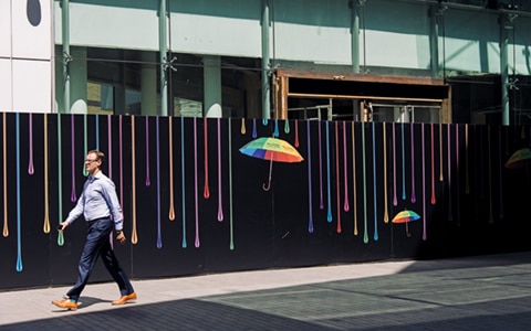 man walking in front of modern art wall with umbrella and paint