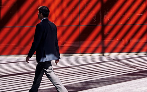 man walking past red wall with strong shadow lines