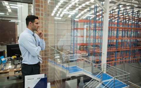 Man standing in glass office overlooking a factory